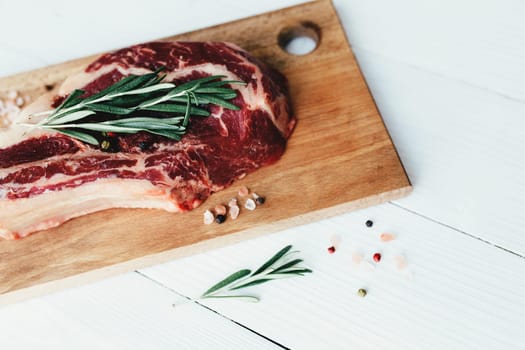 Raw ribeye steak on board, pepper, rosemary and pink Himalayan salt. High quality photo
