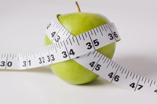 Close_up of a tape measure wrapped around a green apple