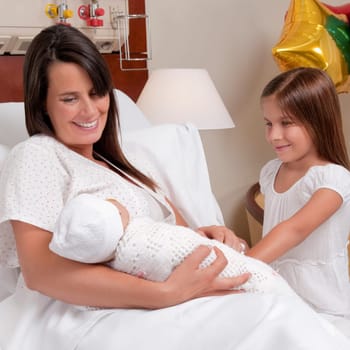 Woman carrying her newborn baby with her daughter in a hospital