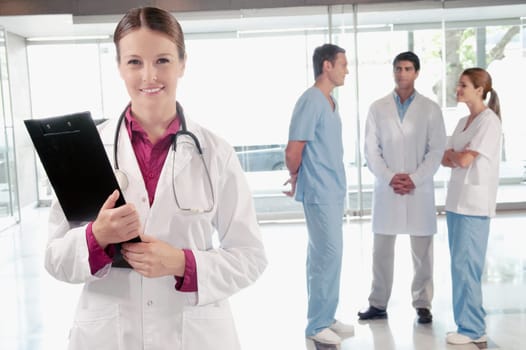 Female doctor holding a clipboard with her colleagues discussing in the background