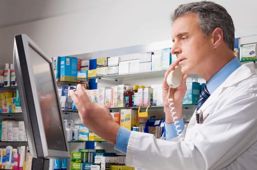 Male pharmacist holding a medicine bottle and talking on the telephone