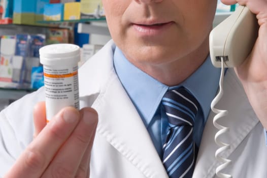 Pharmacist holding a medicine bottle and talking on the telephone