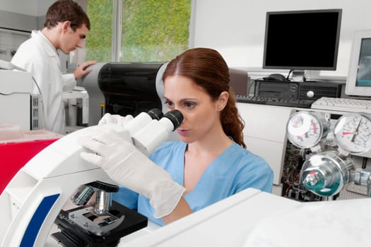 Female lab technician analyzing a sample through a microscope