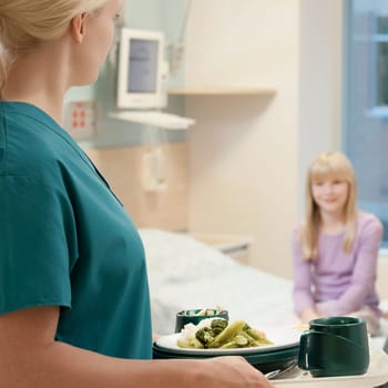 Female nurse holding meal with a patient in the background