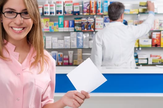 Female pharmacist holding a prescription and a male pharmacist in the background