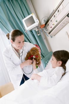 Girl on a hospital bed with a female doctor examining a stuffed toy