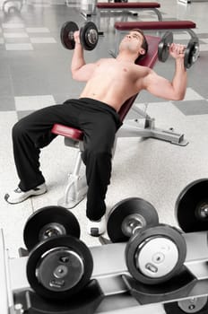 Man lying on a weight bench and exercising with dumbbells