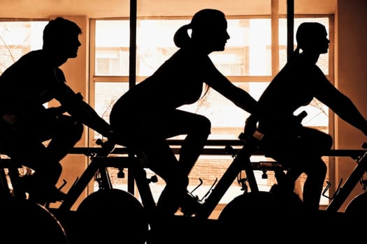 Silhouette of three people working out on exercise bikes in a gym