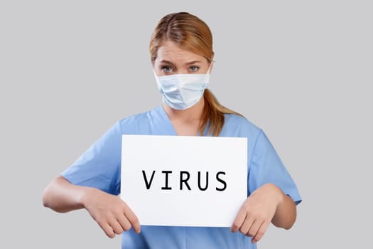 Female nurse wearing a flu mask holding placard with word VIRUS written on it