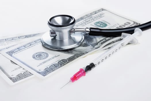 Close_up of hundred dollar bills with a stethoscope and a syringe
