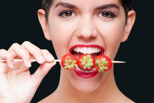 Close_up of a woman biting strawberries on a skewer
