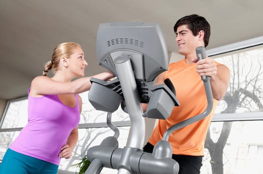 Woman talking to a man working out on a stepping machine in a gym