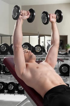 Man lying on a weight bench and exercising with dumbbells