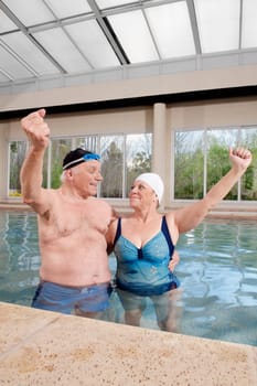 Couple smiling in a swimming pool with their hands raised