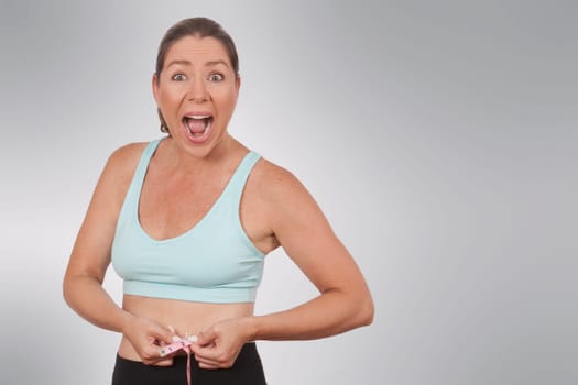 Woman looking surprised while measuring her waist with a tape measure