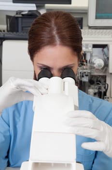 Female lab technician analyzing a sample through a microscope