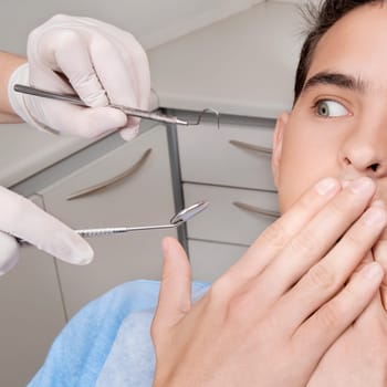 Dentist holding dental equipments while scared patient covering his mouth