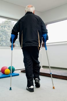 Rear view of a disabled man walking with the help of crutches
