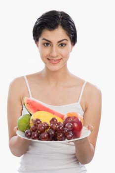 Portrait of a woman holding a plate of assorted fruits