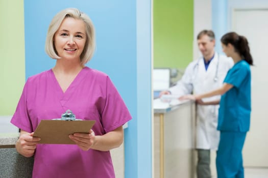 Female nurse holding a clipboard with a doctor and a nurse in the background