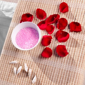 High angle view of bath salt and rose petals with shells on a bamboo mat