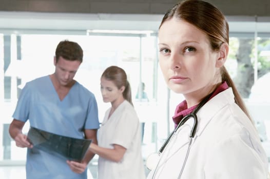Portrait of a female doctor with her colleagues examining an X_Ray in the background