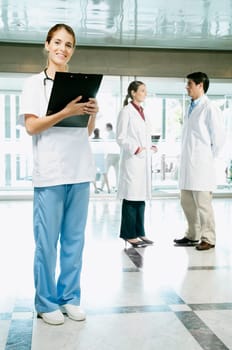 Female nurse holding a clipboard with her colleagues discussing in the background