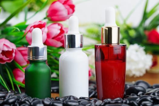 Thai Spa massage setting with serum oil bottle dropper mock up or essential oil on black stone against flower background
