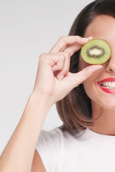 Woman holding half a kiwi over her eye