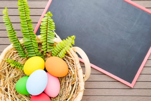 Colorful easter eggs in the basket and blackboard on wood background with space