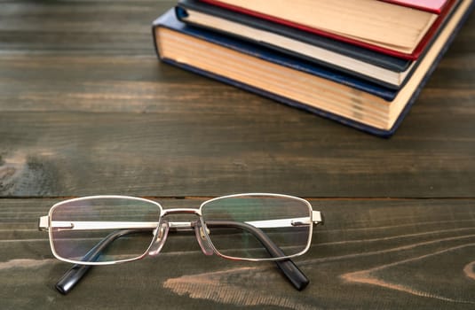 Glasses and stack of hardcover books over wooden table