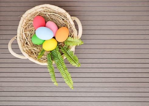Colorful easter eggs in the basket on wood background with space