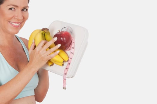 Woman holding a bathroom scale and fruits