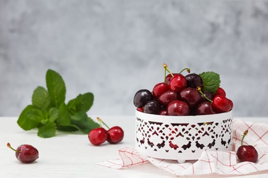 Fresh sweet cherries bowl with meant leaves in water drops on white wooden table. .