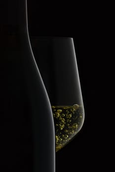 Closeup of bottle and wineglass with white wine on black background.