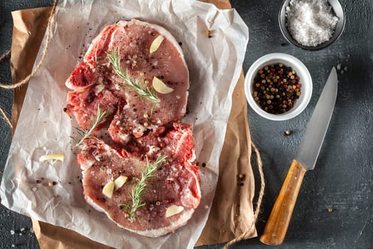 Two raw pork steaks grey stone background with rosemary and spices. Top view, copy space..