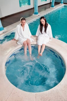 Two women sitting at the poolside with their feet soaking in water