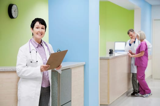 Female doctor holding a clipboard with a doctor and nurse in the background