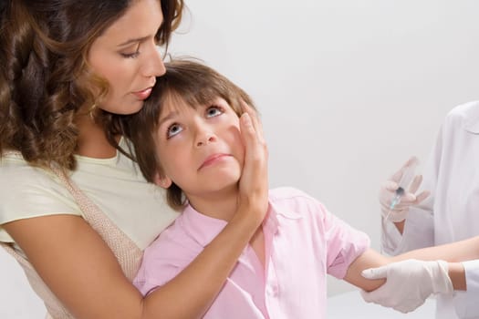 Boy looking at his mother while a doctor injecting him