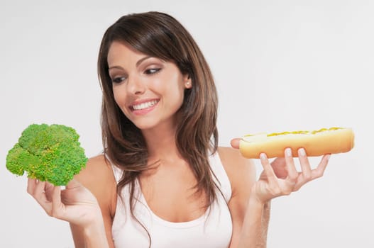 Woman choosing between broccoli and a hot dog