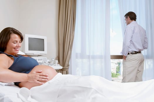Pregnant woman in a hospital with her husband looking out through a window