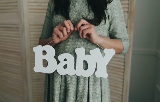 Pregnant woman holding wooden word baby. Waiting for a baby. High quality photo
