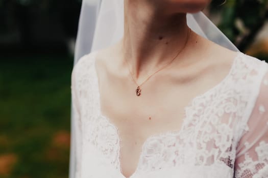 Gold pendant around the neck of the bride in a white dress with veil. Blurred background. High quality photo