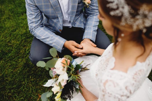 Bride in white dress is holding wedding bouquet. Blurred background. Groom is holding her hand. High quality photo