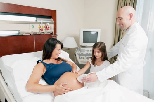 Pregnant woman going through an ultrasound scan with her daughter looking at her