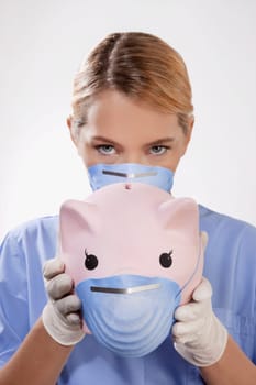 Female doctor wearing a flue mask and showing a piggy bank