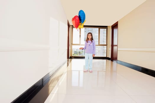 Girl standing with balloons in the corridor of a hospital