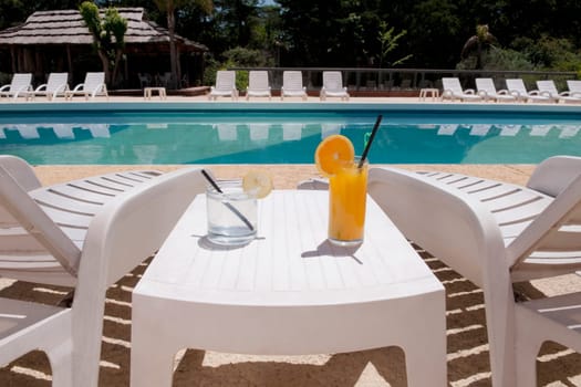 Lounge chairs with juices on table at the poolside