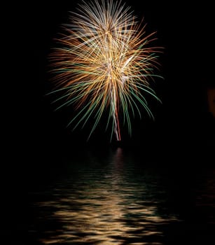 Exploding fireworks with reflexes on water at night