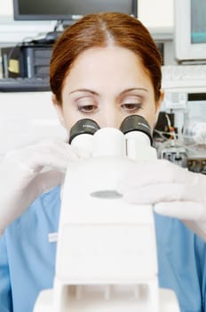 Female lab technician analyzing a sample through a microscope